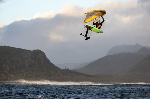Duotone Unit D/LAB foilwing durante salto aereo nel wing foiling sull'oceano con montagne sullo sfondo