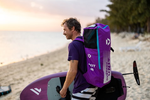 Borsa Duotone Unit per wing foiling indossata come zaino su una spiaggia tropicale al tramonto