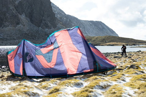 Duotone Dice SLS LEI kite during kitesurfing at a rocky lakeside with snow-dusted mountains