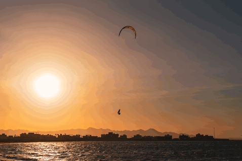 Duotone Rebel SLS LEI kite durante il kitesurf su lungomare urbano con montagne sullo sfondo