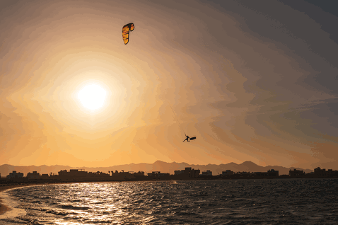 Duotone Rebel SLS LEI kite durante il kitesurf su una spiaggia oceanica con sfondo montuoso