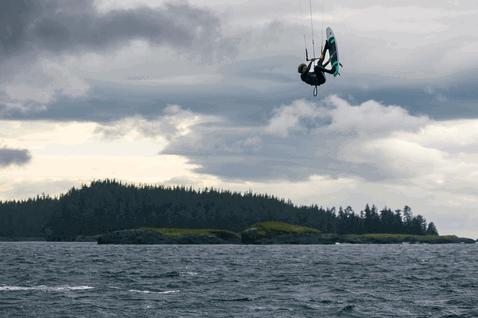 Duotone Rebel SLS LEI kite durante il kitesurf sull'oceano aperto con isola boscosa sullo sfondo
