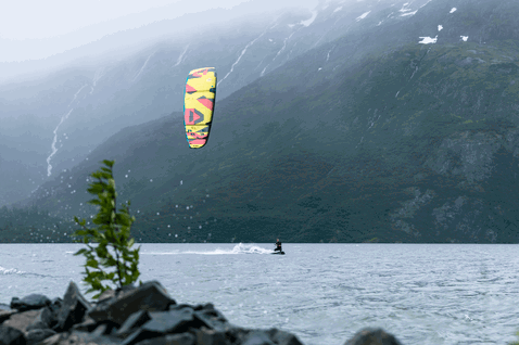 Duotone Rebel SLS LEI kite 8m durante kitesurf su lago di fiordo circondato da montagne e foresta
