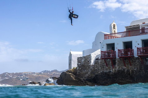 Duotone Jaime SLS twin-tip kiteboard during kitesurfing at a Mediterranean coastal cliff with whitewashed Greek-style building