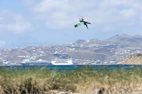 Duotone Select twin-tip kiteboard durante il kitesurf su una spiaggia costiera con villaggio collinare