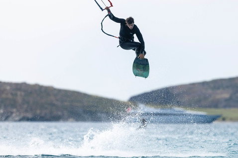 Duotone Select twin-tip kiteboard durante il kitesurf in una baia con colline verdi