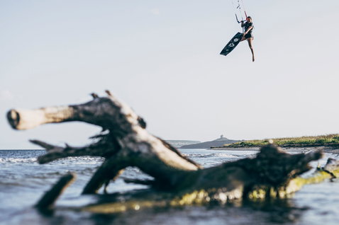 Duotone Soleil twin-tip kiteboard during kitesurfing at a coastal lagoon with driftwood, Sardinia