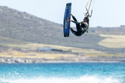 Duotone Kiteboarding Select SLS twin-tip kiteboard during kitesurfing at an ocean beach with hilly coastline