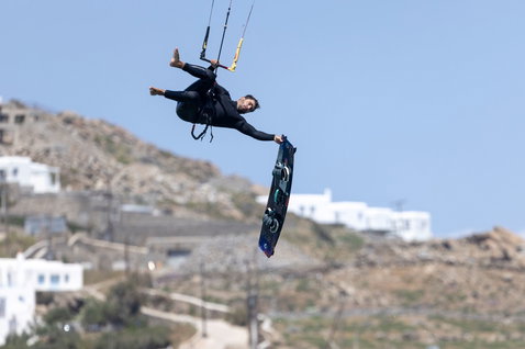 Duotone Select SLS twin-tip kiteboard during kitesurfing at a coastal village with rocky hillside and white buildings