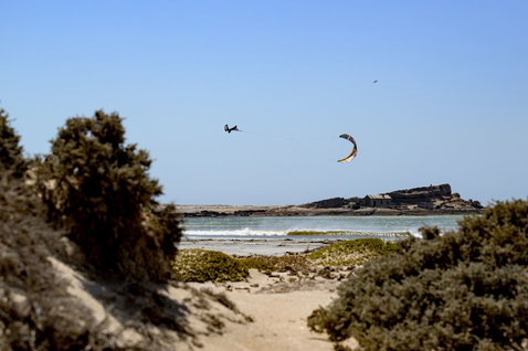 Duotone Evo D/LAB LEI kite during kitesurfing at a rocky coastal beach with scrubland, likely Namibia