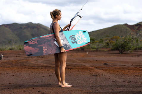 Duotone Gonzales Twin-Tip Kiteboard beim Kitesurfen an einem tropischen Strand mit roter Erde und grünen Bergen