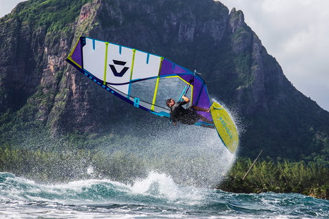 Duotone FreeWave SLS windsurf board during wave riding on the ocean with dramatic mountain backdrop at Le Morne, Mauritius