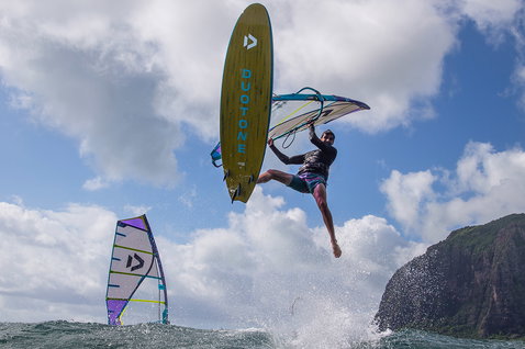 Duotone FreeWave SLS 2024 windsurf board during wave riding in the ocean at a tropical coastline with cliffs