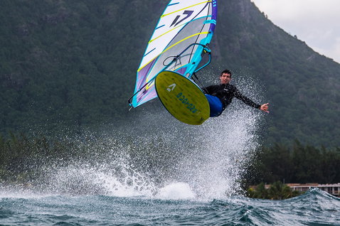 Duotone FreeWave SLS windsurf board during wave riding in an ocean bay with forested mountains