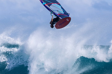 Duotone Grip 3 SLS planche de windsurf lors du surf de vagues dans l'océan en bleu marine avec bleu ciel et rouge