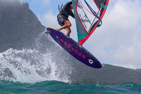 Duotone Skate SLS windsurf board during freestyle windsurfing on the ocean coast with dramatic cliff backdrop