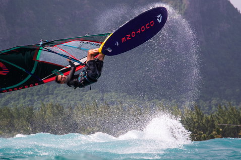 Duotone Skate SLS windsurf board during freestyle windsurfing in a tropical ocean bay with mountain backdrop