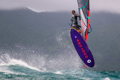 Duotone Skate SLS windsurf board during freestyle windsurfing on a lake with mountainous backdrop