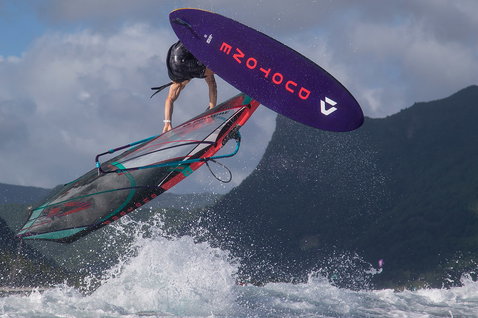Duotone Skate SLS windsurf board during freestyle windsurfing on the ocean coast with mountain backdrop