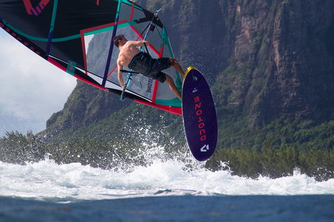 Duotone Skate SLS windsurf board during freestyle windsurfing at a tropical ocean coast with mountainous cliffs