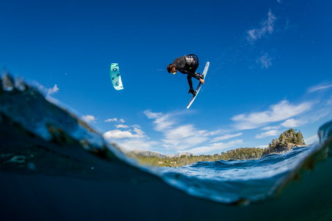Duotone Gambler wake-style kiteboard 151cm during kitesurfing on a lake with forested hills