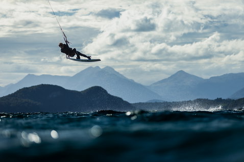 Duotone Gambler twin-tip kiteboard during kitesurfing on the ocean with mountain backdrop