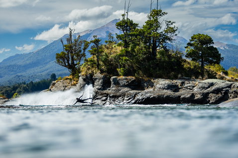 Duotone Gambler wake-style kiteboard during wakestyle riding at an alpine lake with rocky island and mountain backdrop