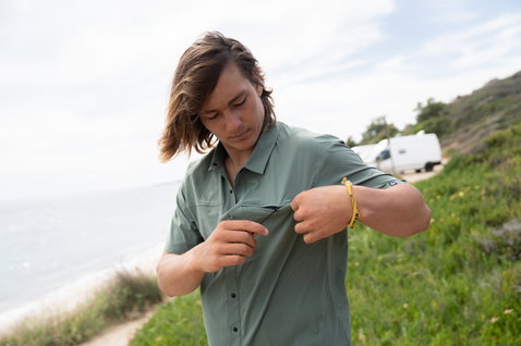 Duotone Apparel Shirt Wave Kurzarmhemd in dusty olive, getragen an küstennahem Hügel mit Meer und Vegetation