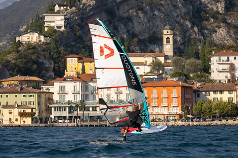 Duotone Warp Foil foil sail during foiling on lake with Mediterranean town and mountain backdrop
