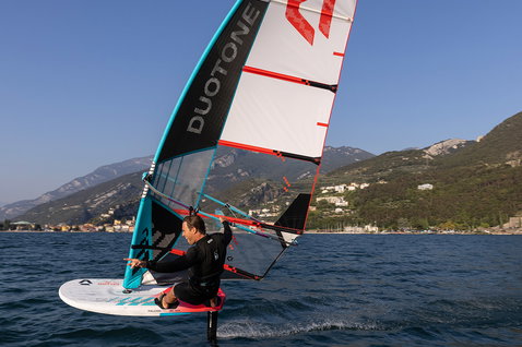 Duotone Warp_Foil foil sail during foiling on an alpine lake with mountains and shoreline