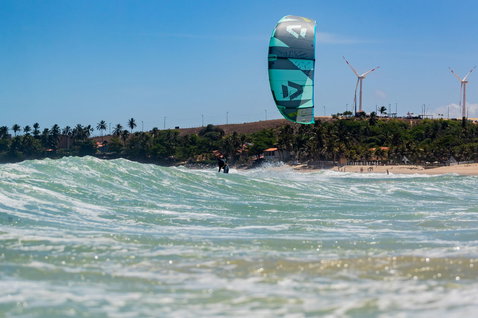 Duotone Evo LEI Kite beim Kitesurfen an einem Ozeanstrand mit Palmen und Windrädern
