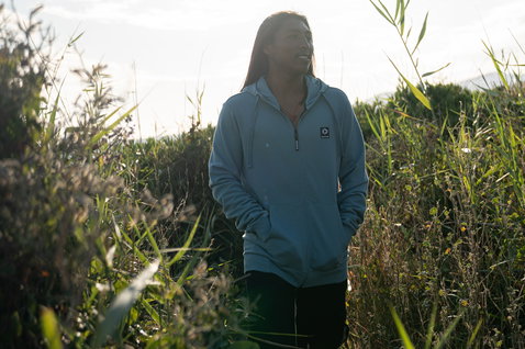 Zip-up hoodie in light blue while posing in coastal grassland
