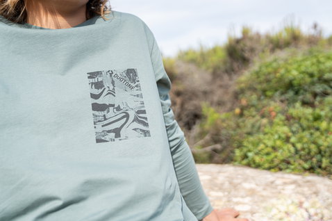 Camiseta de manga larga Duotone Kiteboarding Tee Team LS en verde salvia en una colina costera rocosa