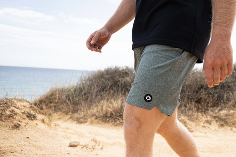 Duotone Boardshorts DT 17inch Herren beim Spazieren am Küstenstrand mit Sanddünen und Ozean im Hintergrund