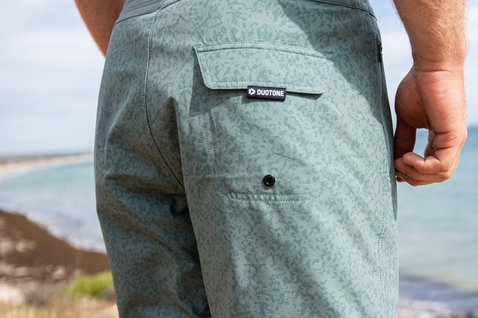 Duotone Boardshorts DT 17inch Herren in salbeigrün mit dunkelgrauem Bund am Ozeonstrand mit Felsen