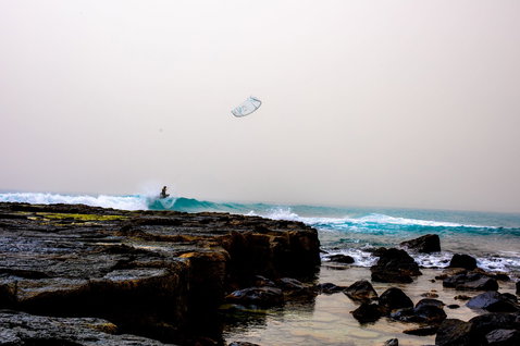 Duotone Neo Concept Blue LEI kite during wave riding at a rocky ocean coastline