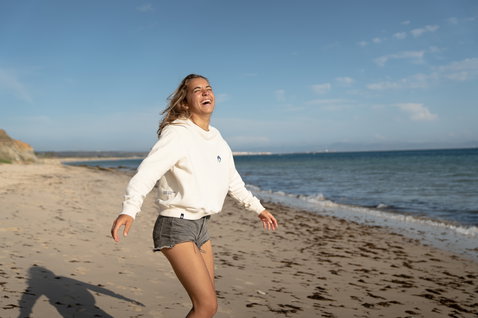 Duotone Apparel Sweater Draft Undyed Women sweat à capuche lors d'une pose sur la plage de l'océan en blanc naturel