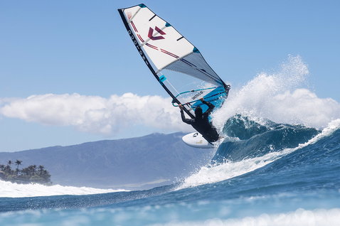 Duotone Super Hero D/LAB wave sail during wave riding on an ocean beach with tropical mountains