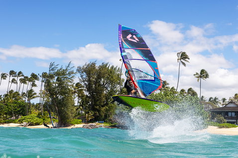Planche de windsurf Duotone Ultra FreeWave SLS lors du surf de vagues dans une baie tropicale avec plage bordée de palmiers