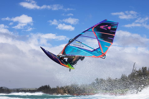 Duotone Duke wave sail during wave riding at an ocean coast with tree-lined shore in background