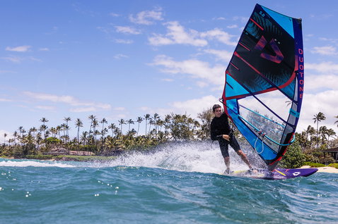 Duotone Duke wave sail during wave riding at a tropical ocean beach with palm trees