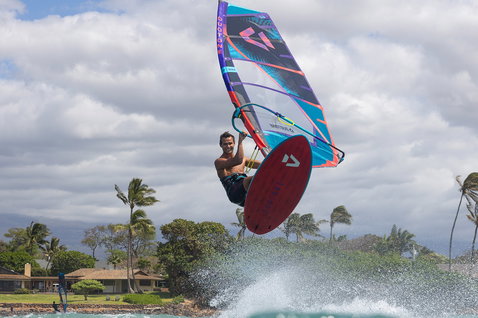 Duotone Ultra FreeWave windsurf board during wave riding at a tropical coastal beach with palm trees and ocean
