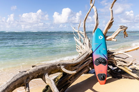 Duotone Ultra FreeWave 2025 windsurf board at a tropical ocean beach with driftwood and turquoise water
