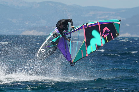 Planche de windsurf Duotone Skate SLS lors de windsurf freestyle en océan ouvert avec des montagnes côtières en arrière-plan