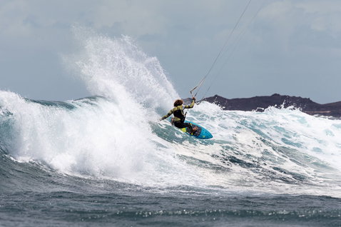 Duotone Dice SLS LEI kite lors du surf de vagues sur une plage océanique avec cap rocheux