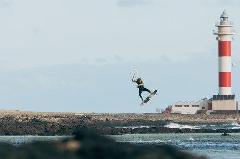 Duotone Whip D/LAB kite surfboard during kitesurfing at a rocky coastline with lighthouse