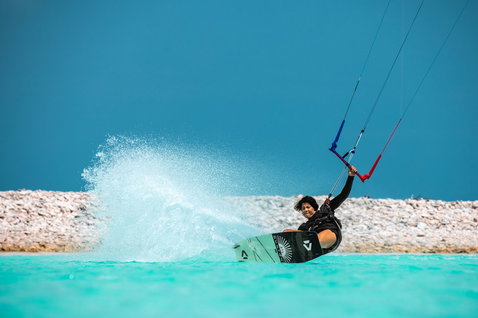 Duotone Soleil SLS twin-tip kiteboard during kitesurfing in a shallow turquoise lagoon with rocky shoreline