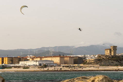 Duotone TS Big Air SLS twin-tip kiteboard during kitesurfing at a coastal town with sandy beach and mountains in the background