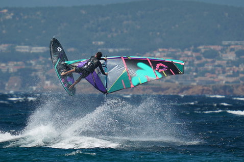Duotone Idol LTD voile de vague en train de rider des vagues sur l'océan avec une ville côtière en arrière-plan