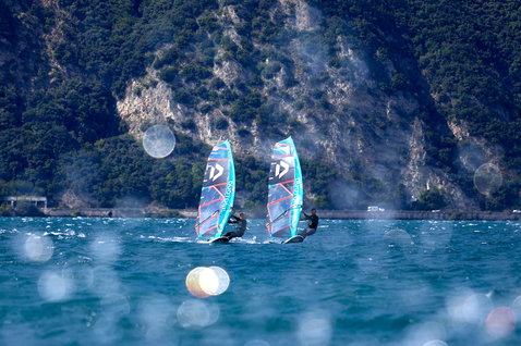Duotone Warp Fin race sail during windsurfing on an alpine lake with rocky mountain backdrop